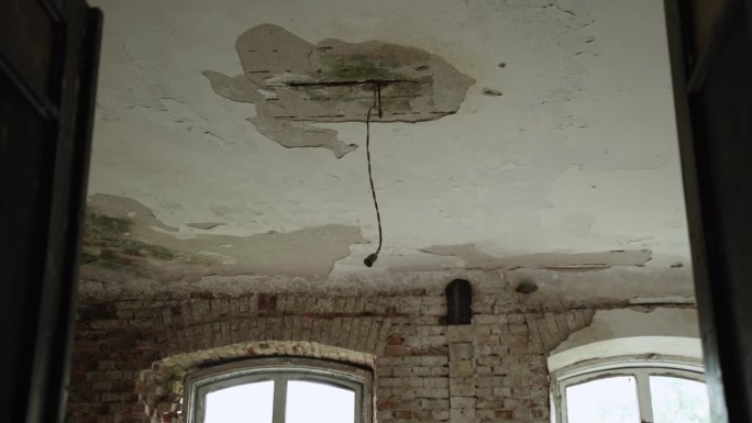 带有空灯泡插座的电线悬挂在破旧的天花板上，灰泥已碎。