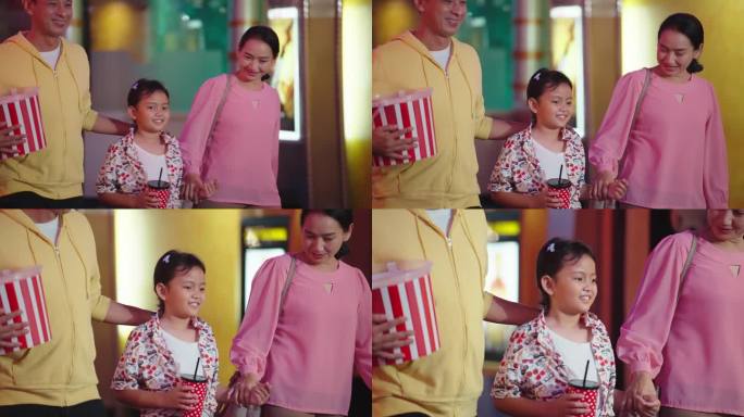 快乐的亚洲女孩和父母拿着碳酸饮料和爆米花桶周末去电影院看电影。快乐的亚洲家庭准备一起去电影院看电影