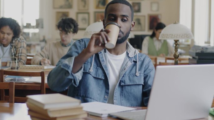 大学生，非裔美国人，在图书馆用笔记本电脑工作，喝着外带咖啡
