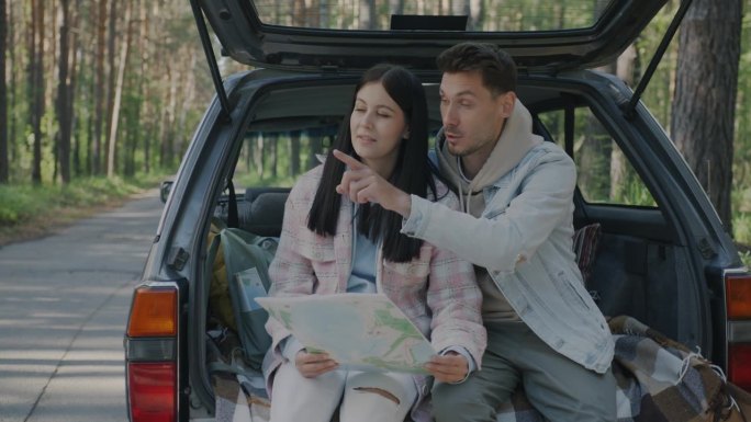 一个男人和一个女人坐在乡下的车里看着地图，指着周围，说话的慢动作肖像