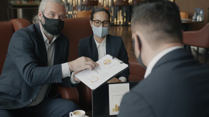 商业伙伴戴着医用口罩在酒店大堂讨论财务文件