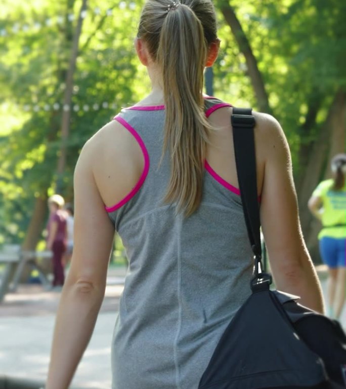 垂直画面:慢动作的运动女子在公园里提着包