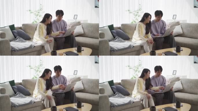 一对韩国夫妇在他们时髦的家中分享微笑。年轻英俊的男人和迷人的女人用笔记本电脑与朋友在社交媒体上进行虚