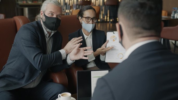 大流行期间，戴口罩的男女在酒店大堂讨论业务