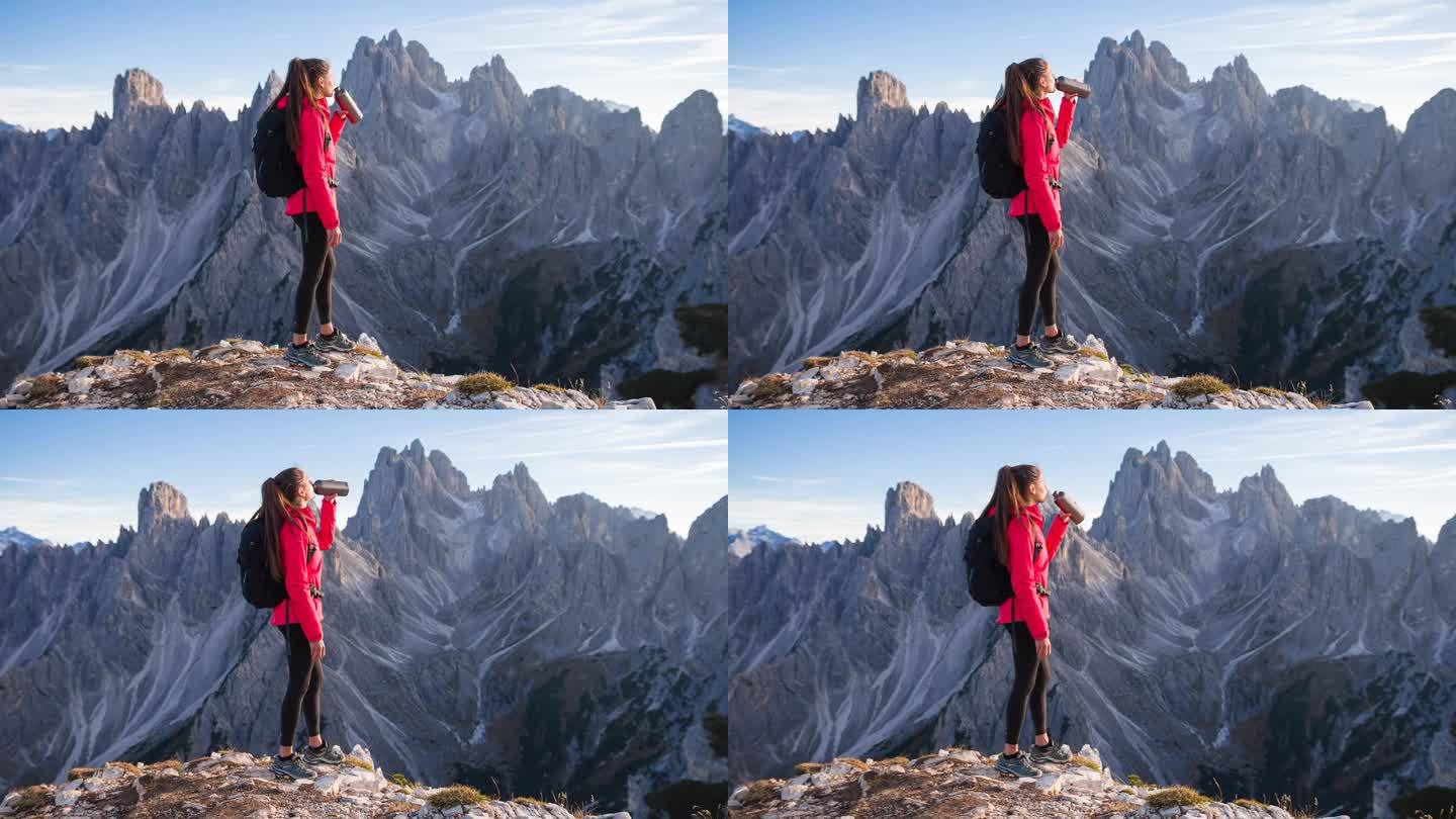 女人在山腰喝水，雄伟的山脉在背后