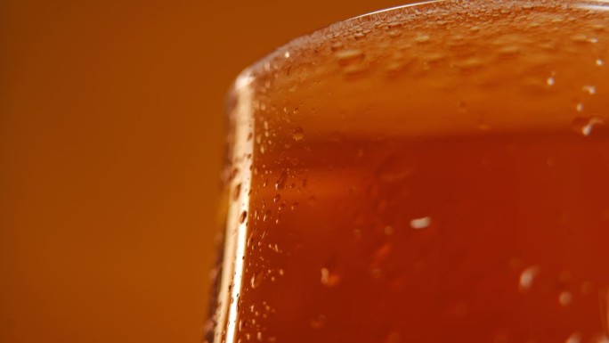 特写部分的啤酒杯与饮料在橙色的背景在右边。清凉酒精饮料广告。