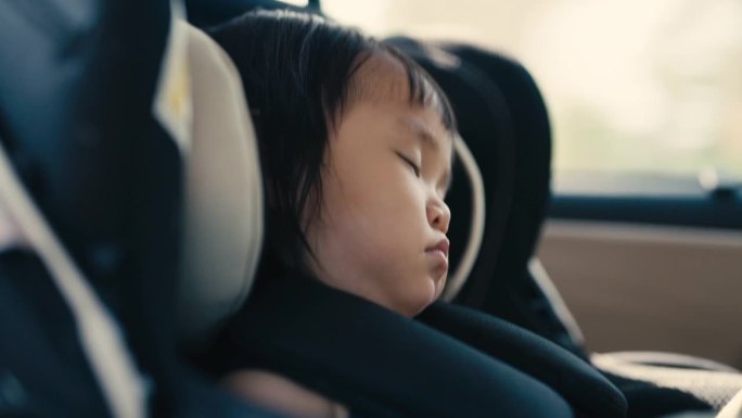 当家人在路上时，亚洲小孩睡在汽车座椅上