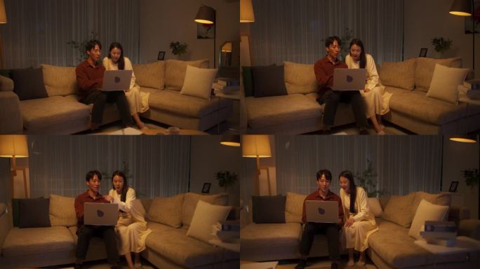 年轻可爱的韩国夫妇晚上用笔记本电脑，在网上为他们时尚的家购物，坐在客厅的沙发上选择购买选项