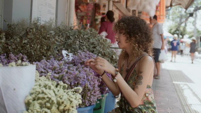 度假时，年轻的女游客在市集花店前欣赏美丽的鲜花。