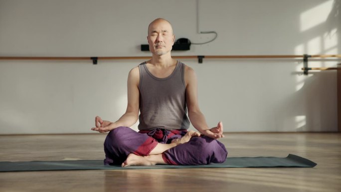 亚洲秃顶男子穿着舒适的衣服，以莲花姿势坐着冥想