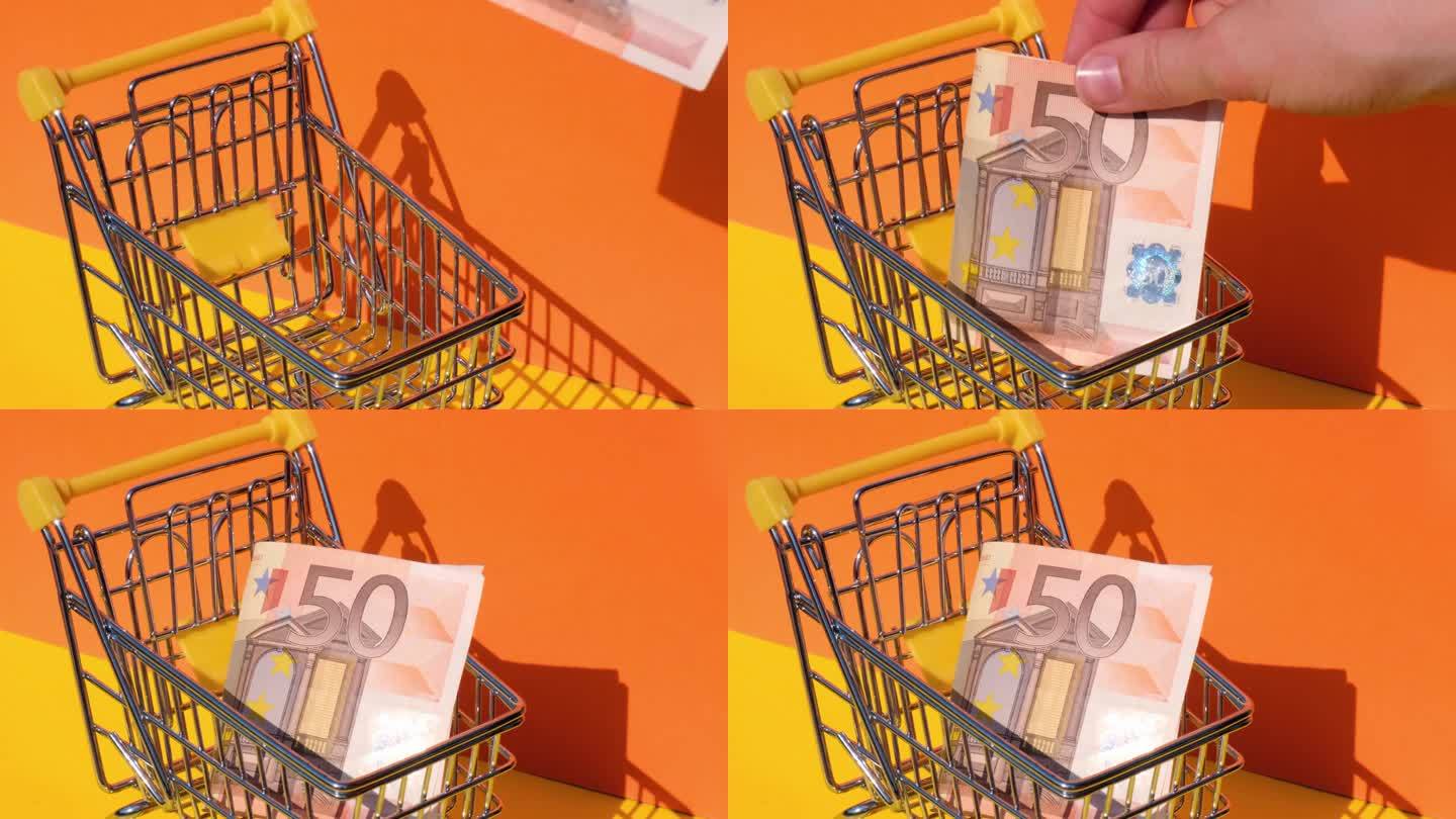 手加50欧元钞票在玩具超市购物车黄色背景的钱。销售一篮子欧元票据。最低生活工资概念:贷款、投资养老、