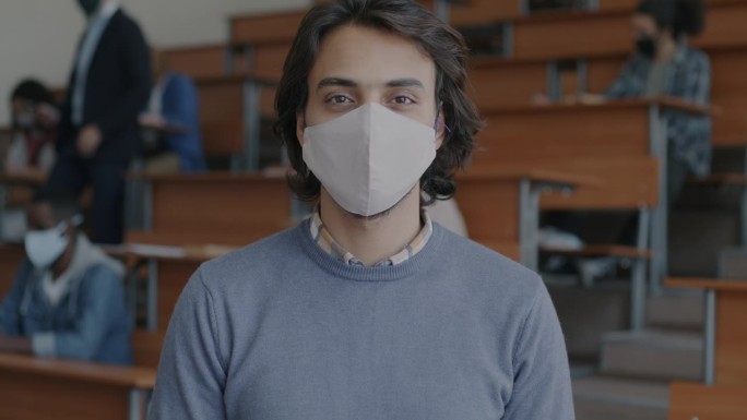 为了预防冠状病毒感染，阿拉伯男学生站在大学礼堂里戴着口罩的慢动作肖像