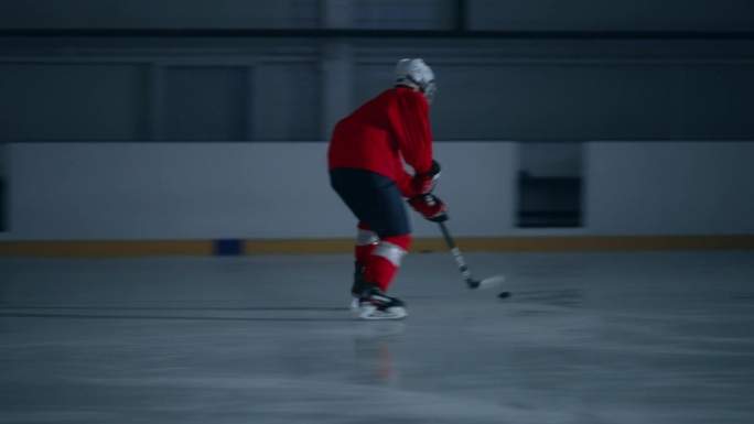 一名身穿红色球衣的冰球运动员在黑暗的冰场上训练的动态视频，展示了令人印象深刻的速度和进球