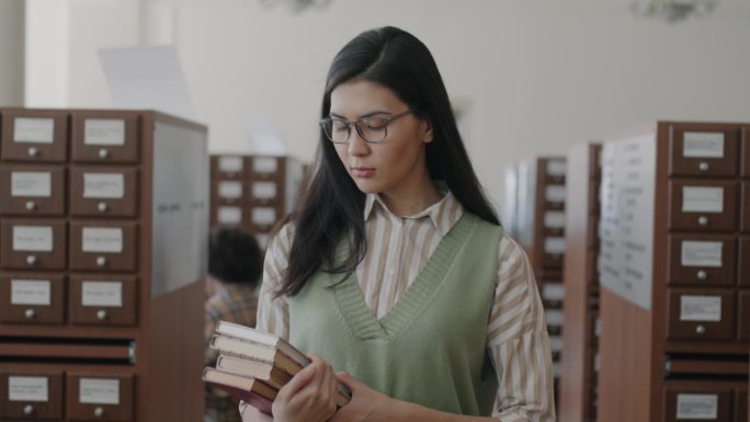 多莉拍摄的亚洲女学生戴眼镜走在大学图书馆拿着书