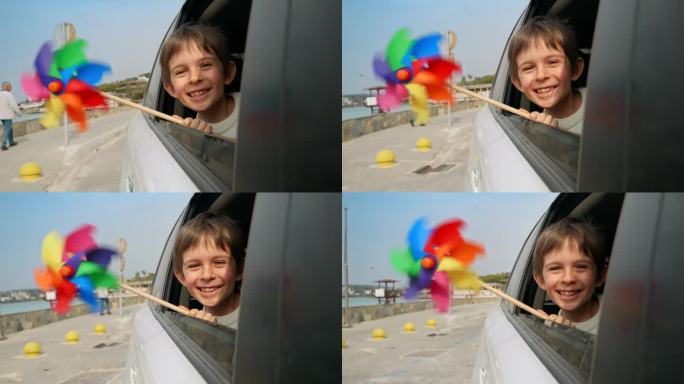 微笑的男孩看着打开的车窗，手里拿着彩色的纺车，因为风吹。儿童旅游、旅行、旅游、假期、周末和假期的概念
