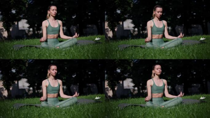 运动的美丽苗条的女人坐在瑜伽垫上莲花的位置在城市公园外。女运动员在阳光明媚的日子里在户外练习瑜伽。莲