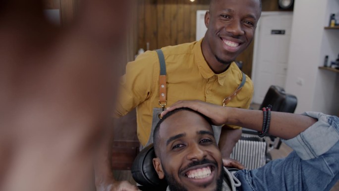 快乐的年轻人客户和理发师在理发店进行在线视频通话，一边聊天一边挥手看着镜头
