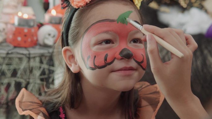 万圣节快乐。妈妈画小女孩的脸，化妆为万圣节不给糖就捣蛋，万圣节化妆，庆祝活动