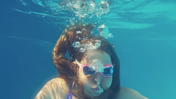 年轻的白人女孩在游泳池里潜水，呼出气泡
