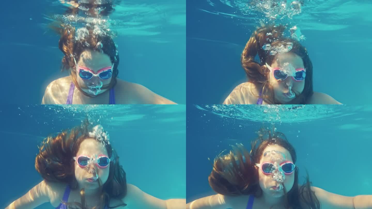 年轻的白人女孩在游泳池里潜水，呼出气泡