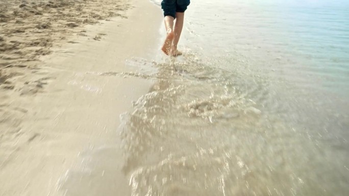 孩子的脚在沙滩上奔跑的特写，平静的海浪中溅起了水。假期，假期，周末在大自然