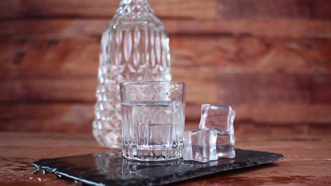 前面的人使溅冰在玻璃杯与清澈的酒，如伏特加或龙舌兰酒，在瓶子前面