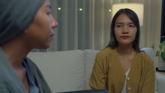 年轻的亚洲人牵手信任安慰帮助癌症患者说话哭泣晚上在家里的客厅减压。医疗保健。