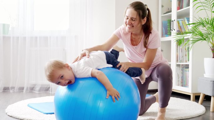 开心微笑的小男孩和妈妈一起躺在健身球上做伸展运动。儿童保健，儿童运动和瑜伽的概念