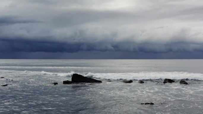 广阔的航拍画面，海浪滚滚涌向海岸，黑暗，戏剧性的风暴云在银色的海洋上移动