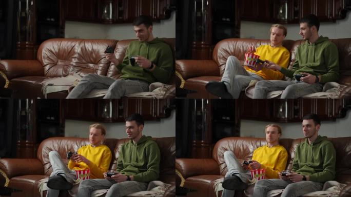 客厅的沙发上，两个男人拿着摇杆和爆米花进来玩电子游戏。积极放松的白人男性玩家享受室内游戏。