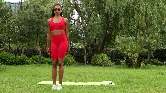 年轻漂亮的运动黑人女性伸展身体，蹲在户外。一个穿着运动服的女孩为了健康而参加户外运动。
