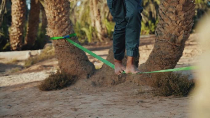 一名赤脚男子在海滩上的棕榈树间走着绳索