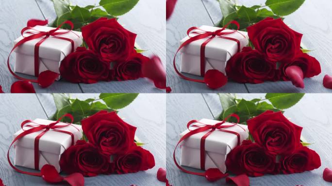 三朵红玫瑰和礼盒放在蓝色的桌子上，花瓣缓缓落下