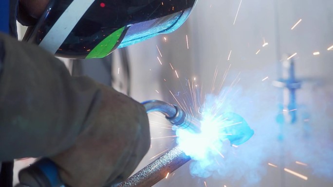 一个蒙面焊工在车间工作，火花四溅。特写肖像。工业背景。视频的工作流程。