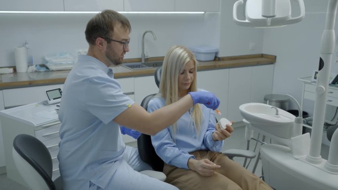 男牙医用模型向女病人讲解如何正确刷牙。健康的生活方式。慢动作