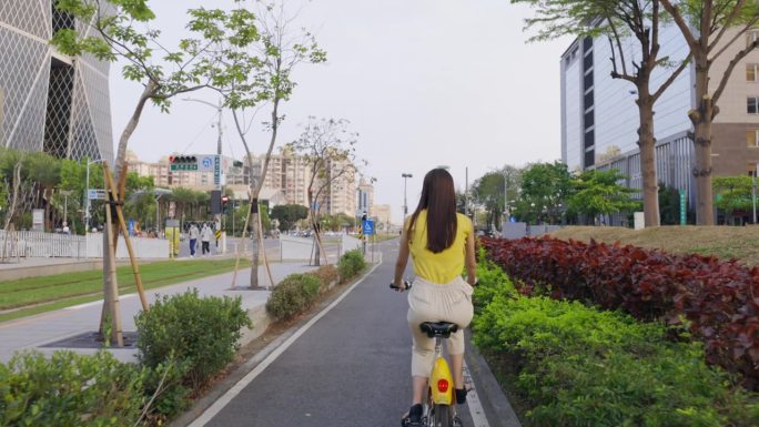 从后景看，一位亚洲妇女骑着自行车在城市中穿行。