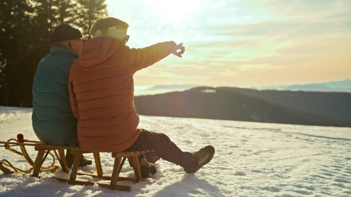 一对老年夫妇在日落时坐在雪橇上欣赏风景
