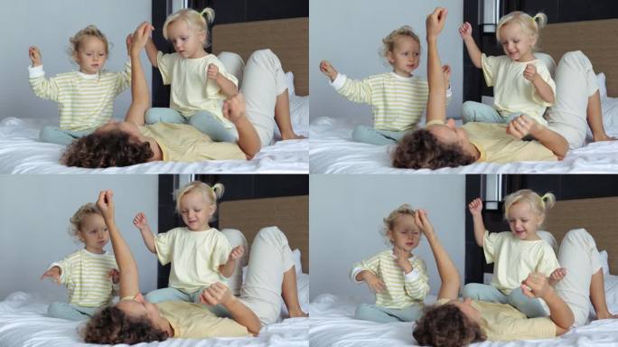 妈妈和女儿在床上手舞足蹈，伴着音乐开怀大笑。妈妈和她心爱的女儿的孩子们玩得很开心，娱乐他们，跳舞，给