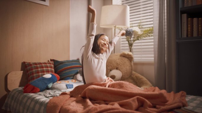 可爱的韩国小女孩在她舒适的房间里睡了一觉后醒来。亚洲小男孩和泰迪熊玩具睡在一起。她还是很困，四处张望