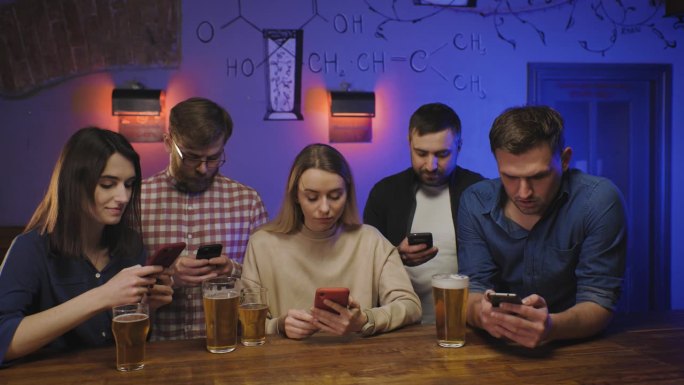 酒吧里的朋友们端着啤酒在吧台边看他们的智能手机。社会生活。现代世界。每个人都盯着自己的手机，刷着社交