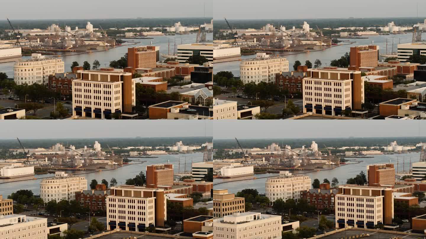 日落时河边的医疗中心大楼。多层建筑高耸的城市景观。远处正在建造军舰的海军造船厂。朴茨茅斯，弗吉尼亚州