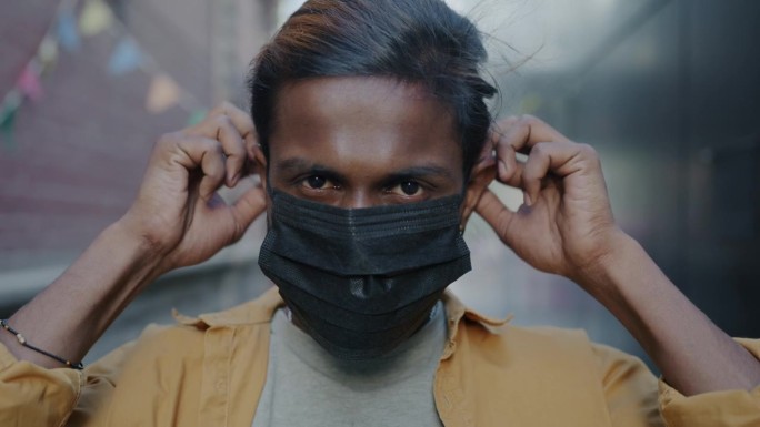 一名严肃的印度男子戴上医用口罩站在城市街道上的慢动作肖像，在covid-19大流行中幸存下来