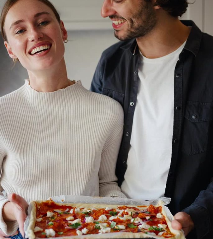 一对夫妇在家里的厨房里拿着准备烤箱的披萨的垂直视频肖像