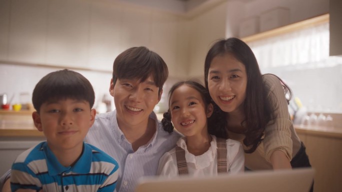 幸福的韩国家庭使用笔记本电脑，然后看着镜头微笑。年轻的父母和两个可爱的孩子一起看他们上次旅行的照片和