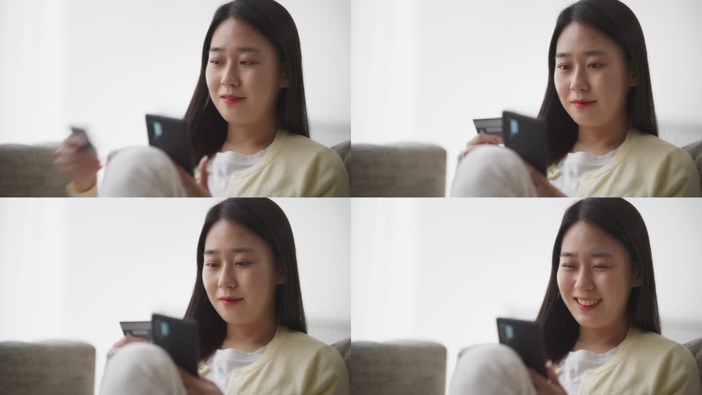 一个漂亮的韩国女性用智能手机拿着信用卡的肖像。亚洲女性做移动购物疗法，在客厅浏览网上购物网站，发现时