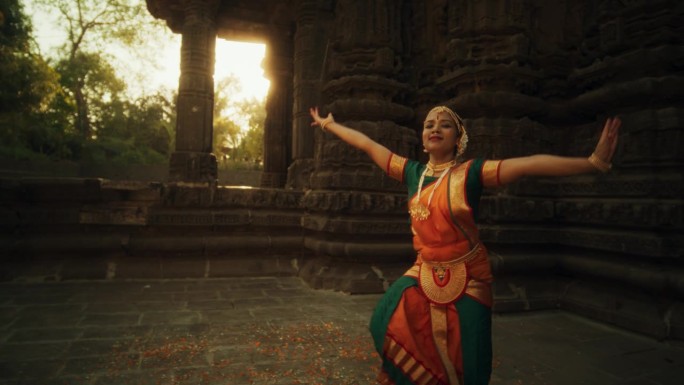富于表现力的年轻女性在庙里跳民间舞蹈编舞的肖像。印度妇女穿着色彩鲜艳的传统服装，美丽而迅速地表演Bh