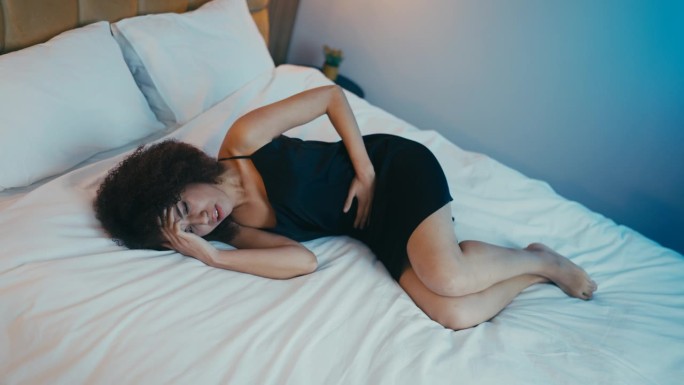 非裔美国妇女胃痛躺在床上，痛经，受伤