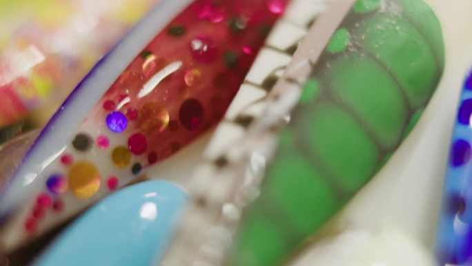 模糊背景拍摄。美甲师向客户展示五颜六色的塑料针尖和个性化设计的指甲。不同的设计，色彩斑斓的艺术闪耀粒