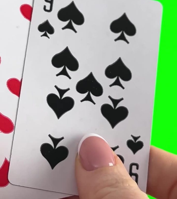 手拿着四个九在绿色背景的特写女性的手与法式美甲。女人整理卡片，检查它们折叠起来，像扇子一样展开同一套