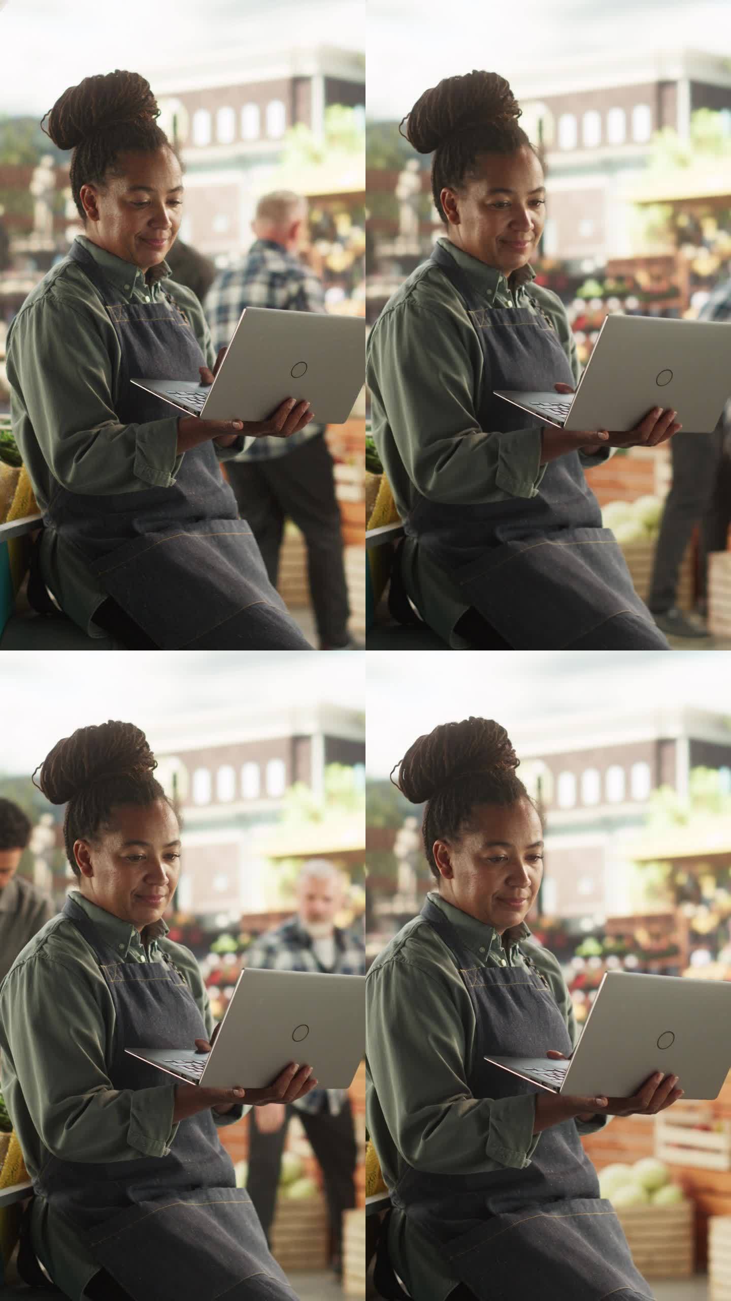 垂直屏幕:多民族非洲女商人在笔记本电脑上工作，为城市广场上的美食节做准备。一位女士坐在有机农产品摊位